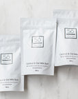 Three packages of Coconut & Oat Milk Bath on a light background with decorative pink and white stones