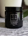 A 100 ml black jar of Só Silver Mission Falls Premium Ionic Silver Gel, placed on a gray and white striped fabric surface with a blurred background.