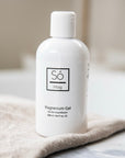 A white bottle of Só Magnesium Gel with on beige fabric with a blurred background.