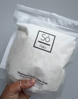 A hand holding up a bag of magnesium bath flake with 'Só Flaky' branding on a gray background