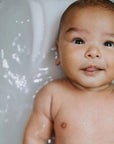 A close-up of a baby laying in a white bathtub with water around them.