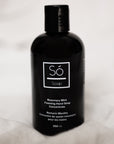 A black bottle of Só Soap foaming hand wash concentrate in Rosemary Mint scent, standing upright styled on a blurry white background.