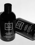 Two black bottles of Só Soap hand wash concentrates, one standing upright and the other lying on its side, on a white background.
