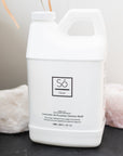 A white bottle labeled 'Só Clean Lavender All Purpose Cleaner', placed on a dark surface with a white and a pink rock in the background