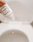 Hand holding a bottle labeled Só No. 2 over a toilet bowl with a drop of product dripping into the toilet.