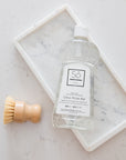 Bottle of branded Só Clean itrus Rinse Aid with a wooden brush on a marble surface