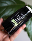 Hand holding a black deodorant stick with 'Só Fresh Extra Strength Limelight" branding against a green leafy blurred background