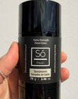 Black deodorant stick with 'Só Fresh Extra Strength Sandstorm' branding held by a hand against a light gray background