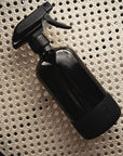 A black glass spray bottle on a rattan surface