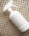 A white glass spray bottle on a rattan surface