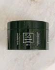 A 250 ml black jar of Só Sweet Bergamot Vanilla body scrub, resting on a light beige marble surface.