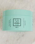 A 250 ml mint green jar of Só Sweet Coco Mint body scrub, resting on a light beige marble surface.