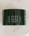 A 250 ml black jar of Só Sweet Lavender Lime body scrub, resting on a light beige marble surface.