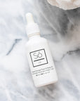 A white bottle with a dropper labeled 'Só Oil Sweet Orange Face & Body Oil' on a grey marble background.