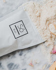 A package of Só Luxury brand Blush soak with a light pink powdered product scattered around, presented on a marble surface with rose petals.