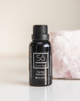 A black bottle of Só Essential Oil labelled Tea Tree 30 ml on a light beige background with pink rock behind.