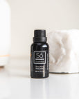 A black bottle of Só Essential Oil labelled Ylang Ylang 30 ml on a light grey background with a white rock in the background.