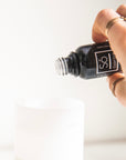 A hand holding a black glass bottle labelled Só Essential Oil over an open essential oil diffuser.