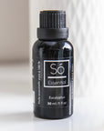 A black bottle of Só Essential Oil labelled Eucalyptus 30 ml with a white pattern and light gray background