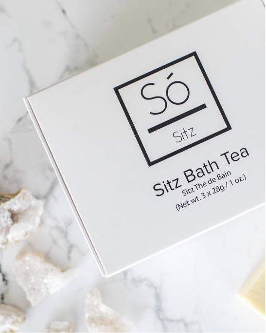 A white rectangular box of Só Sitz Bath Tea with black text, photographed on a white marble surface with a few quartz crystals nearby.