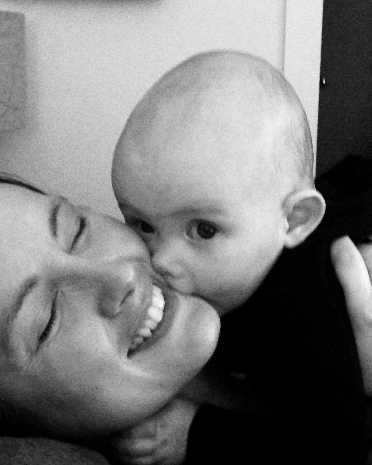 Black and white photo of a woman and a baby kissing mom's face