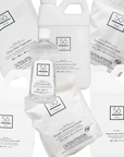 A set of Só Clean laundry and bathroom cleaning products on a white background, including a clear bottle of Citrus Rinse Aid, white refill jugs of Tangerine Dish Soap, Lavender All Purpose Cleaner and Stain Remover and Prewash and white bags of powdered laundry soda, citrus dish capsules and oxygen whitening powder.
