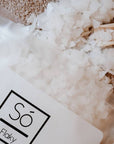 Magnesium flake salt crystals spilling out of a white and frosted bag labeled 'Só Flaky' on a textured surface.