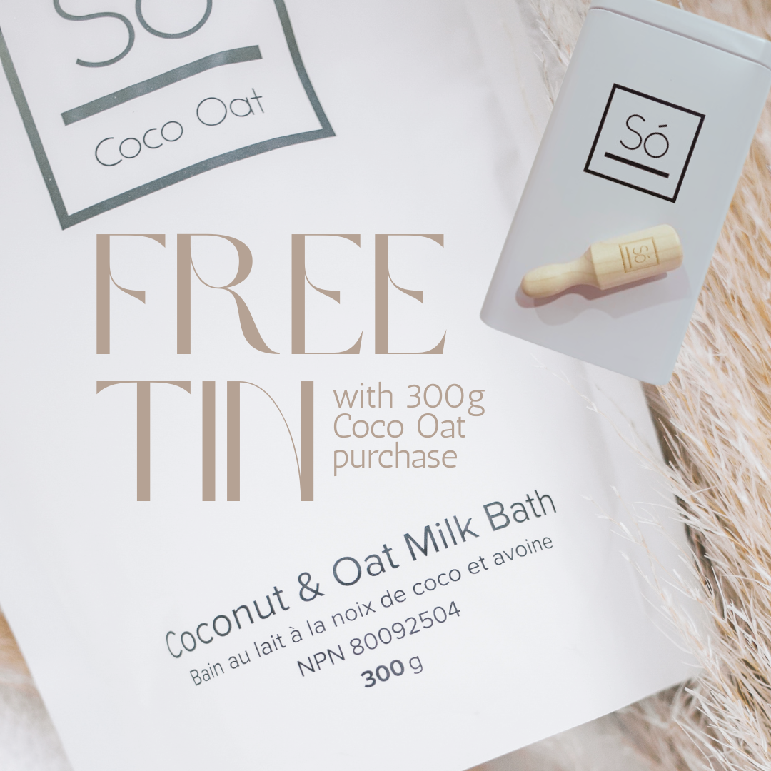 A close-up of a white product package for “FREE TIN” coconut and oat milk bath, with a small white tin shown beside it on a soft beige textured surface. The package text reads “Coconut & Oat Milk Bath,” “300 g,” and the visible brand is “Só