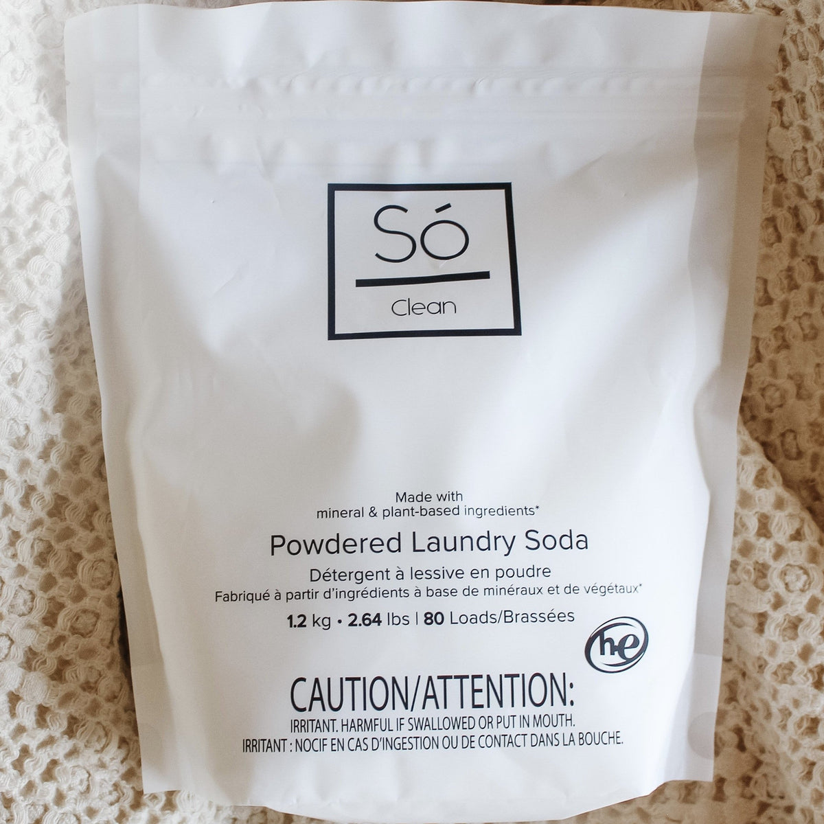 A white bag of Só Clean Powdered Laundry Soda on a textured beige fabric background.