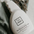 White spray bottle branded with 'Só Clean Stain Remover + Prewash' on a light marble background with green fabric and greenery.