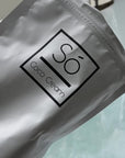 Video showing a Só Coco Cream bath soak being poured into a bath with running water and swirling water showing the product