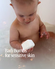 A baby in a bathtub holding a bath bomb with the words Bath Bombs for sensitive skin no fragrance no dyes.