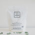 A white package of Só Clean powdered laundry soda with minimalistic design, featuring a black square logo and product information text on a light background with eucalyptus leaves.